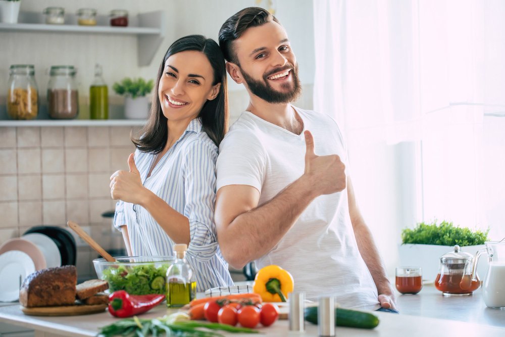 emocionada y sonriente pareja joven enamorada haciendo una ensalada vegana súper saludable en su cocina sostenible