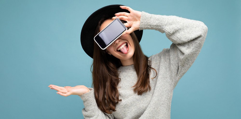 hermosa mujer joven con sombrero negro y suéter gris sosteniendo el teléfono mostrando el teléfono inteligente